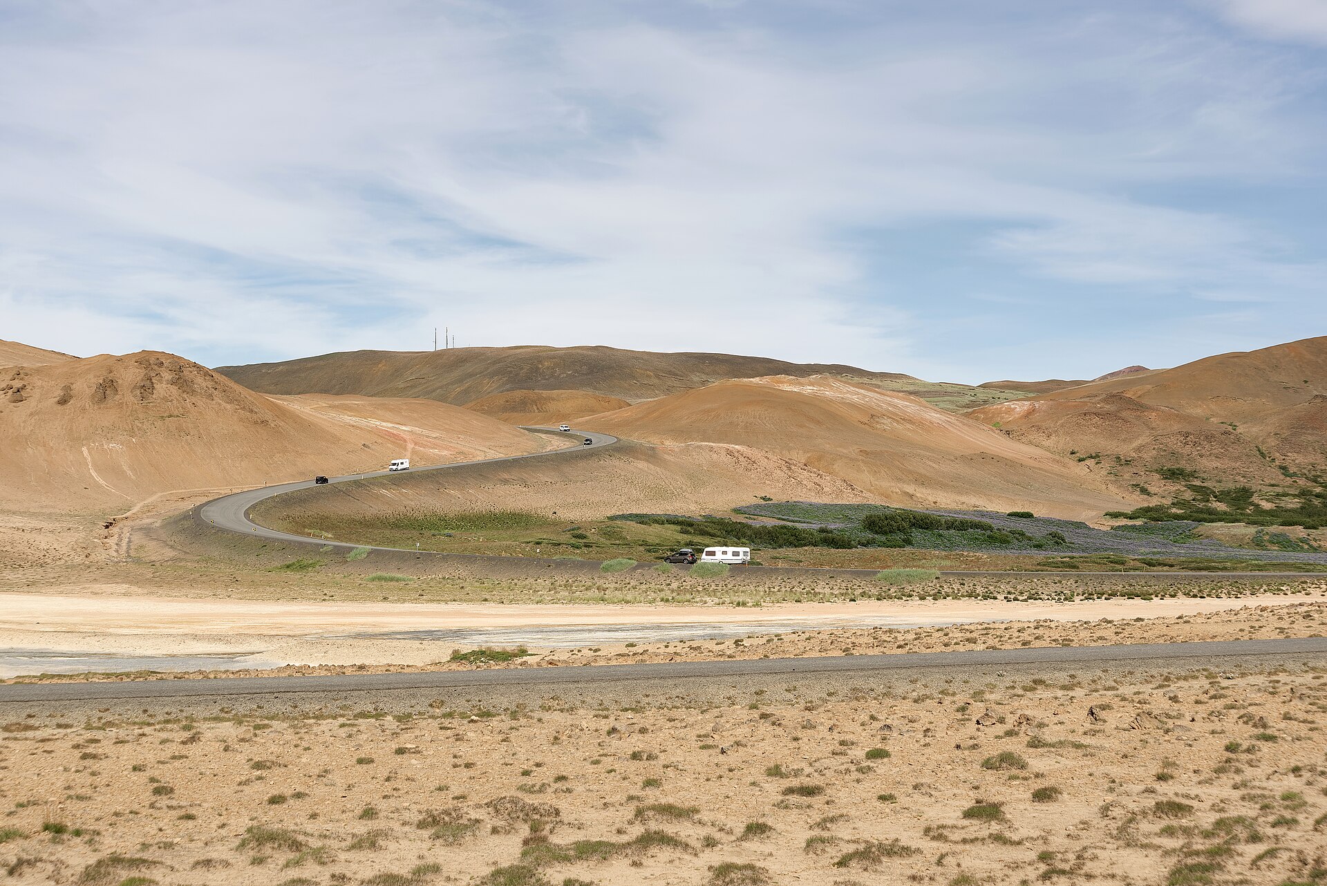 冰島一號公路在赫維拉倫(Hverarönd)附近穿過起伏火山地形,多輛車與露營車正在行駛